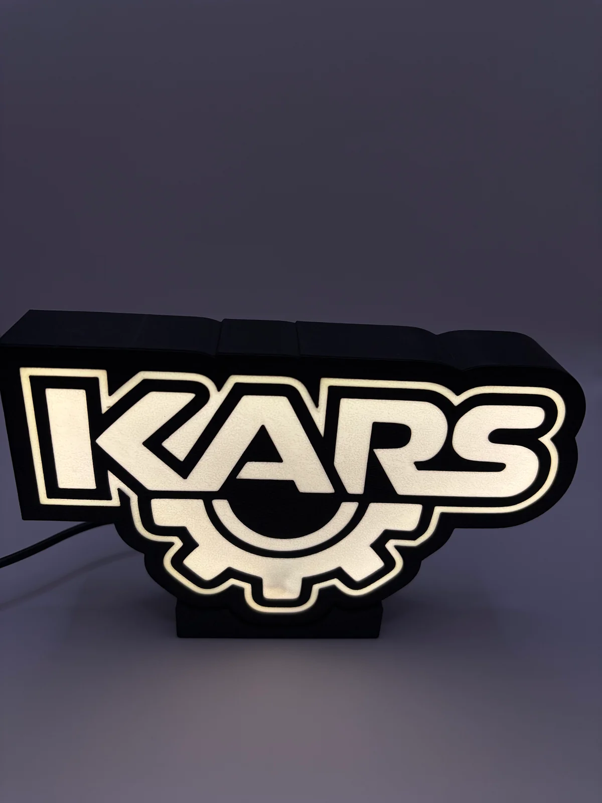Lightbox Kars éclairée, avec lettrage blanc et engrenage dans un boîtier noir.