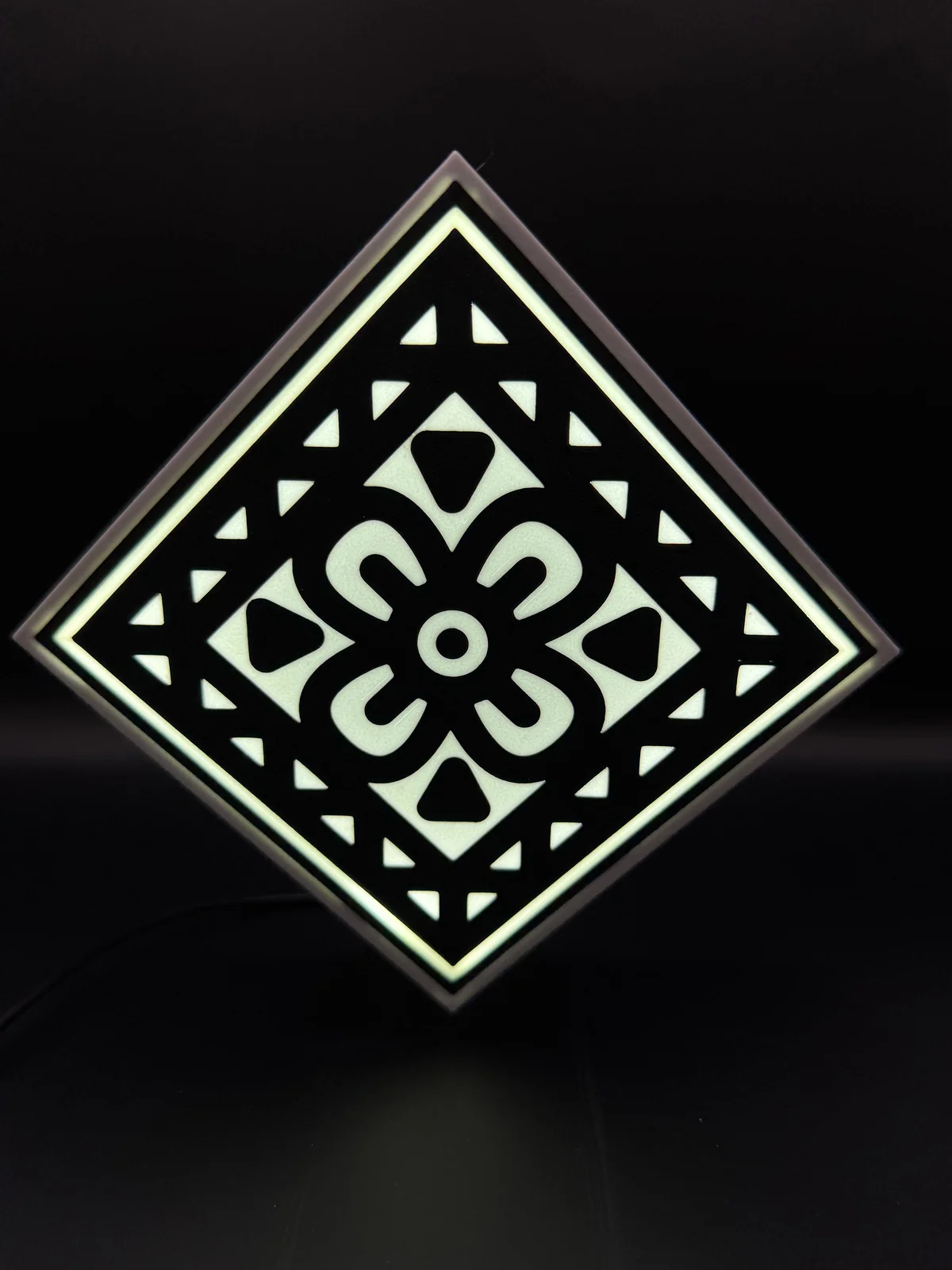 Lightbox O’Zeit en forme de losange, avec motif noir sur fond lumineux blanc.