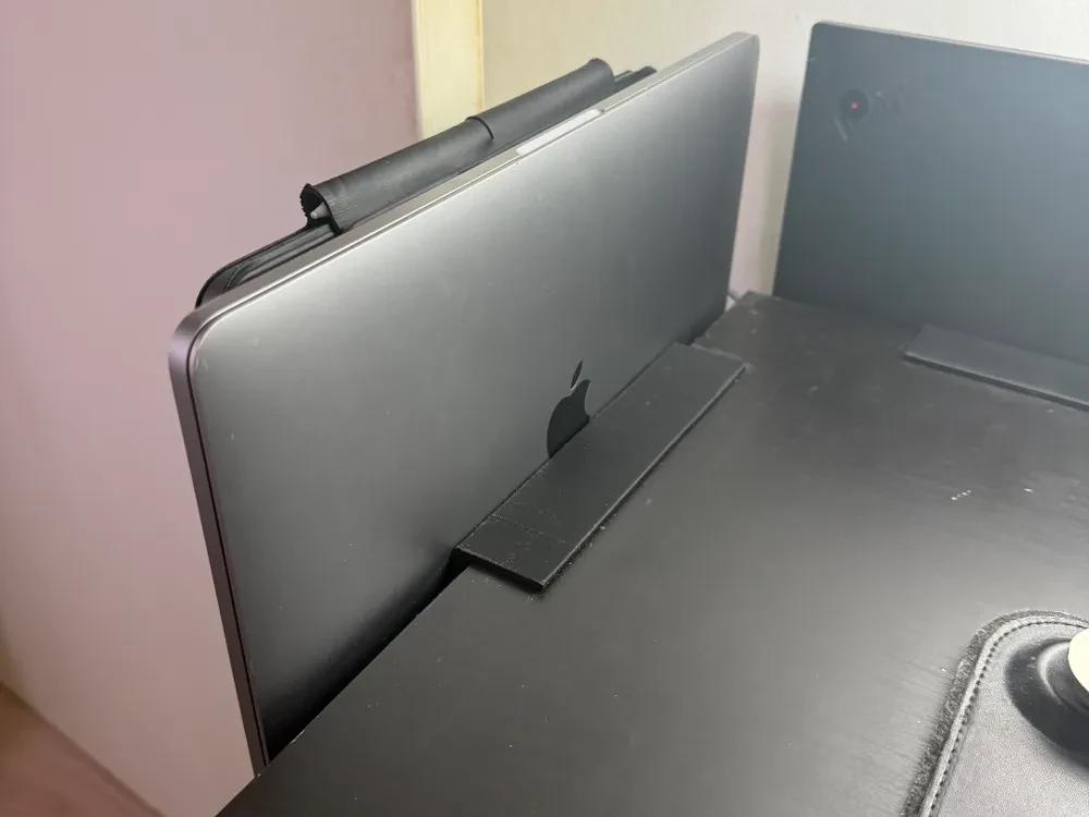 Support noir imprimé en PLA sur le côté du bureau, avec un MacBook et un iPad rangés verticalement.